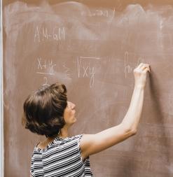 A lecturer writes math formulas with chalk on a brown board.