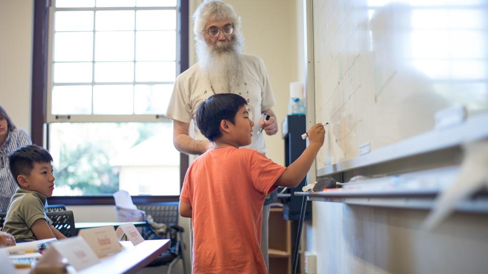 An instructor works with a young student at the whiteboard during a Stanford Math Circle session.